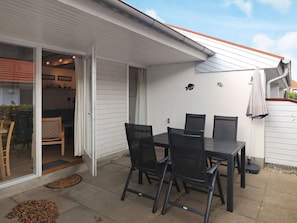 Eine Terrass mit Tisch und Stühlen, eine Glastür, die zu einem Raum führt, und eine kleine Wanddekoration.