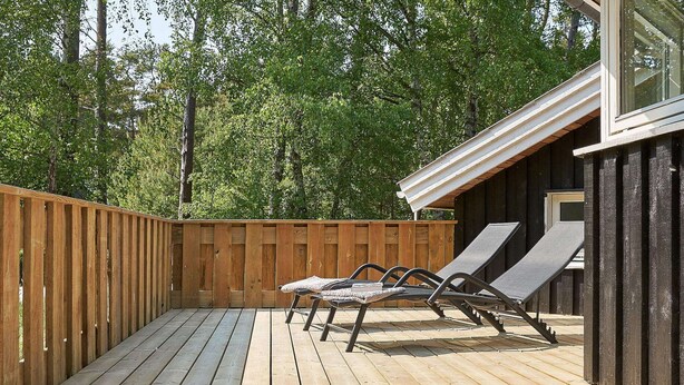 A wooden deck with two lounge chairs and a small building with a window.