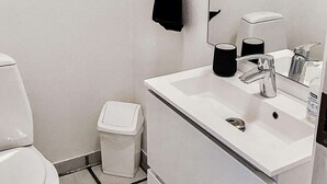 A bathroom with a toilet, a sink, a trash bin, and a mirror.