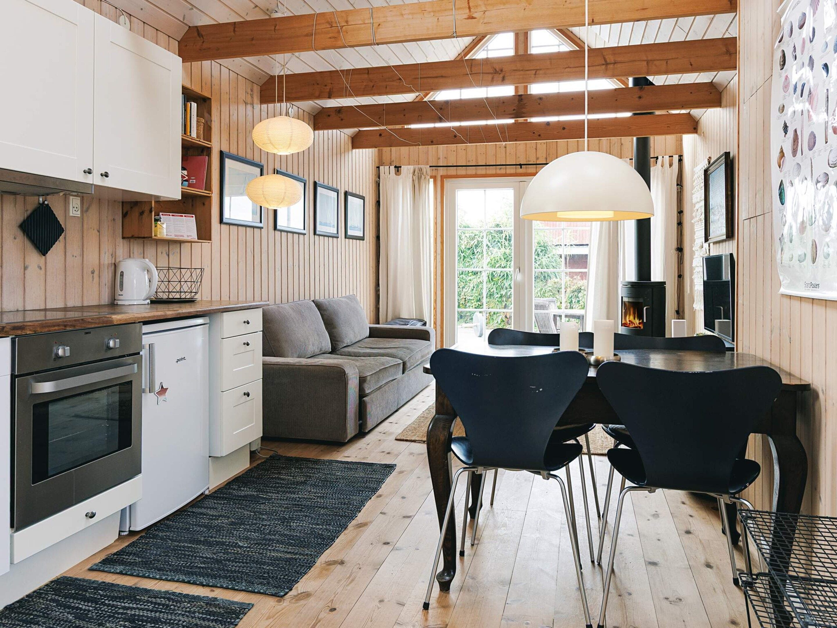 A modern kitchen with wooden beams, a dining area with chairs, a sofa, and a fireplace.