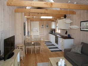 A cozy interior with a wooden dining area, a kitchen with white cabinets, and a living space with a sofa and a flat-screen TV. - 4 Star Holiday Home in Karrebaeksminde (Karrebæksminde)
