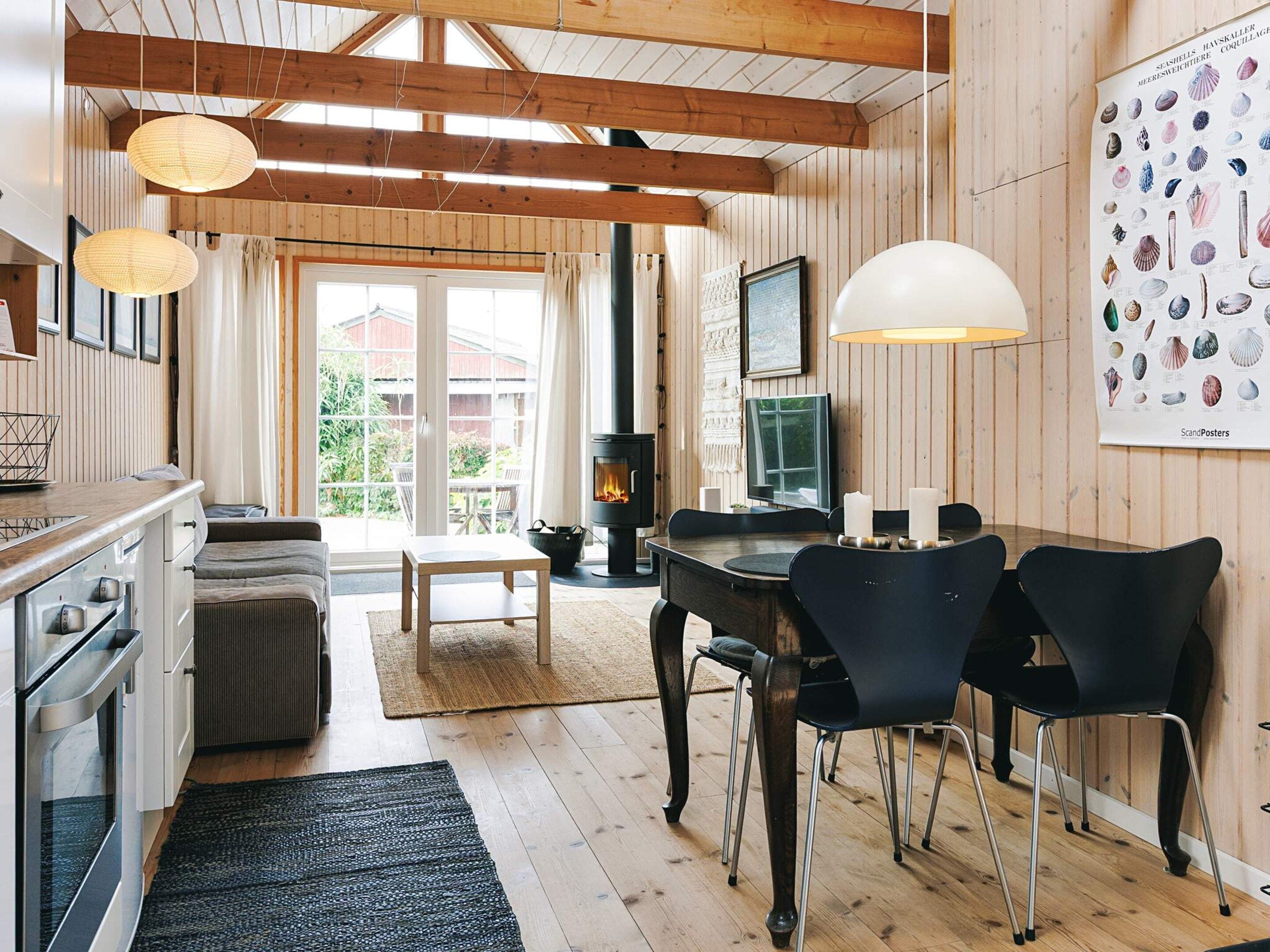 A cozy cabin interior with a wooden dining table, chairs, a fireplace, and a large poster of seashells.