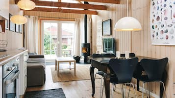 A cozy cabin interior with a wooden dining table, chairs, a fireplace, and a large poster of seashells.