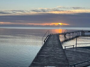 Une jetée en bois s’étendant sur une étendue d’eau calme, avec un coucher de soleil en arrière-plan.