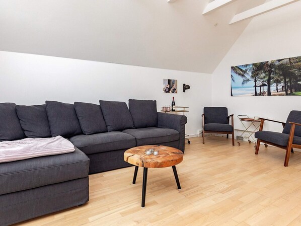 Un salon moderne avec un canapé gris, une table basse en bois et deux fauteuils.