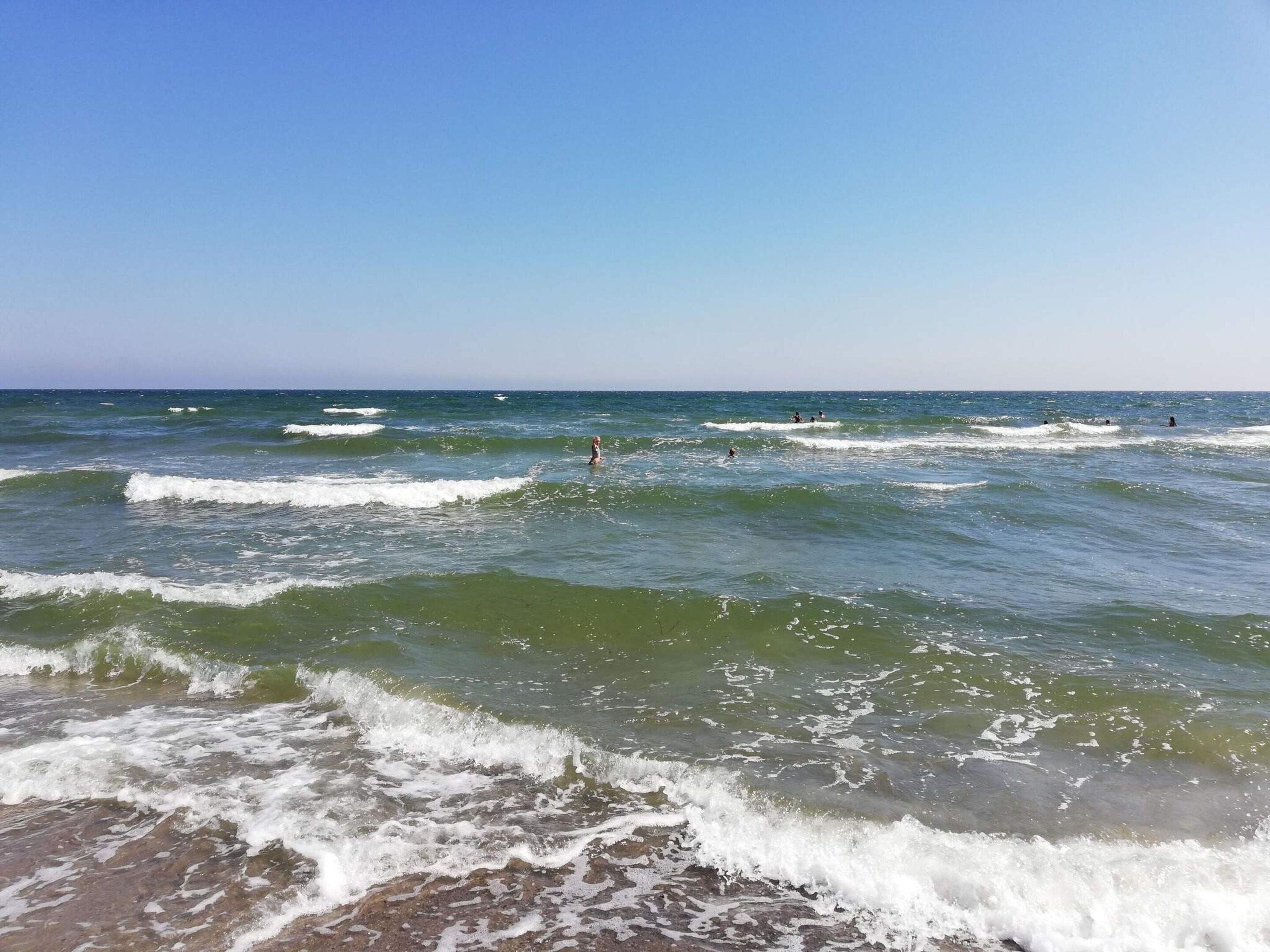 A beach with waves and people in the water.