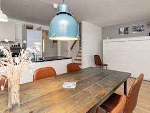 Ein Essbereich mit einem Holztisch, Stühlen, einer blauen Pendelleuchte und einer Vase mit Trockenpflanzen.