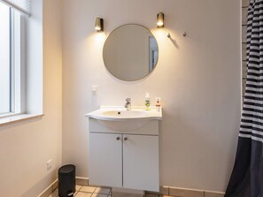 Une salle de bain avec un miroir rond, un lavabo blanc et une poubelle noire.