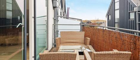 A balcony with wicker furniture, a glass door, and a view of the surrounding buildings.