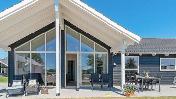 A modern house with a glass-enclosed patio, outdoor seating, and a clear sky.