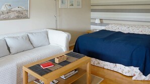 A bedroom with a bed, a sofa, a small table with a book, and a floor lamp. - 4 Person Holiday Home in Tvaaker (Tvaaker)