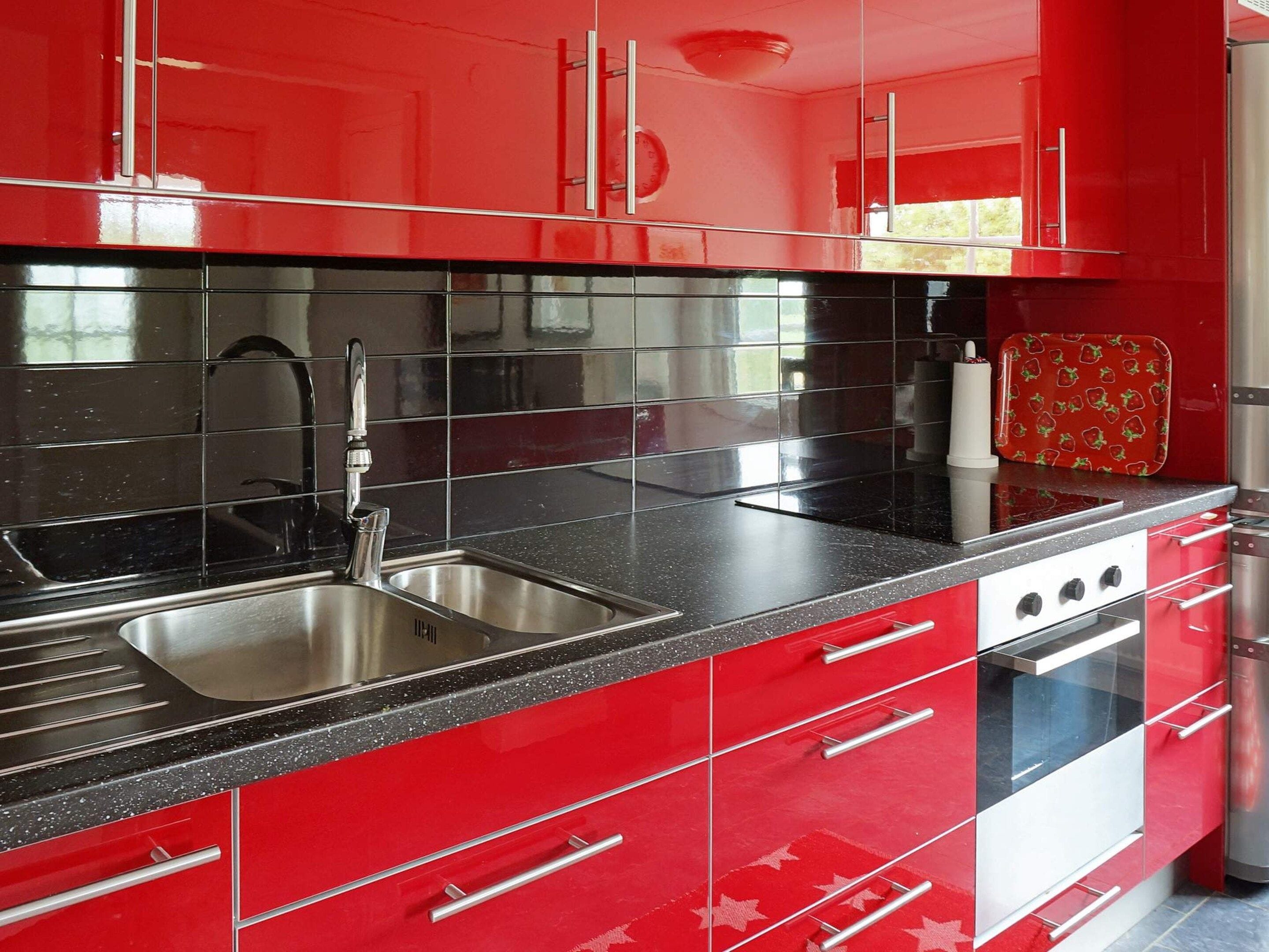 Una cocina moderna con armarios rojos, electrodomésticos de acero inoxidable y encimeras negras.