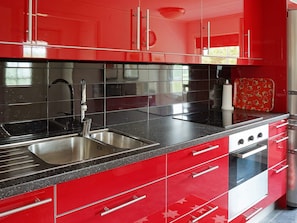 A modern kitchen with red cabinetry, stainless steel appliances, and black countertops.