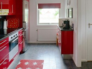A kitchen with red cabinets, a white countertop, and a window with a red valance. - 4 Person Holiday Home in Tvaaker (Tvaaker)