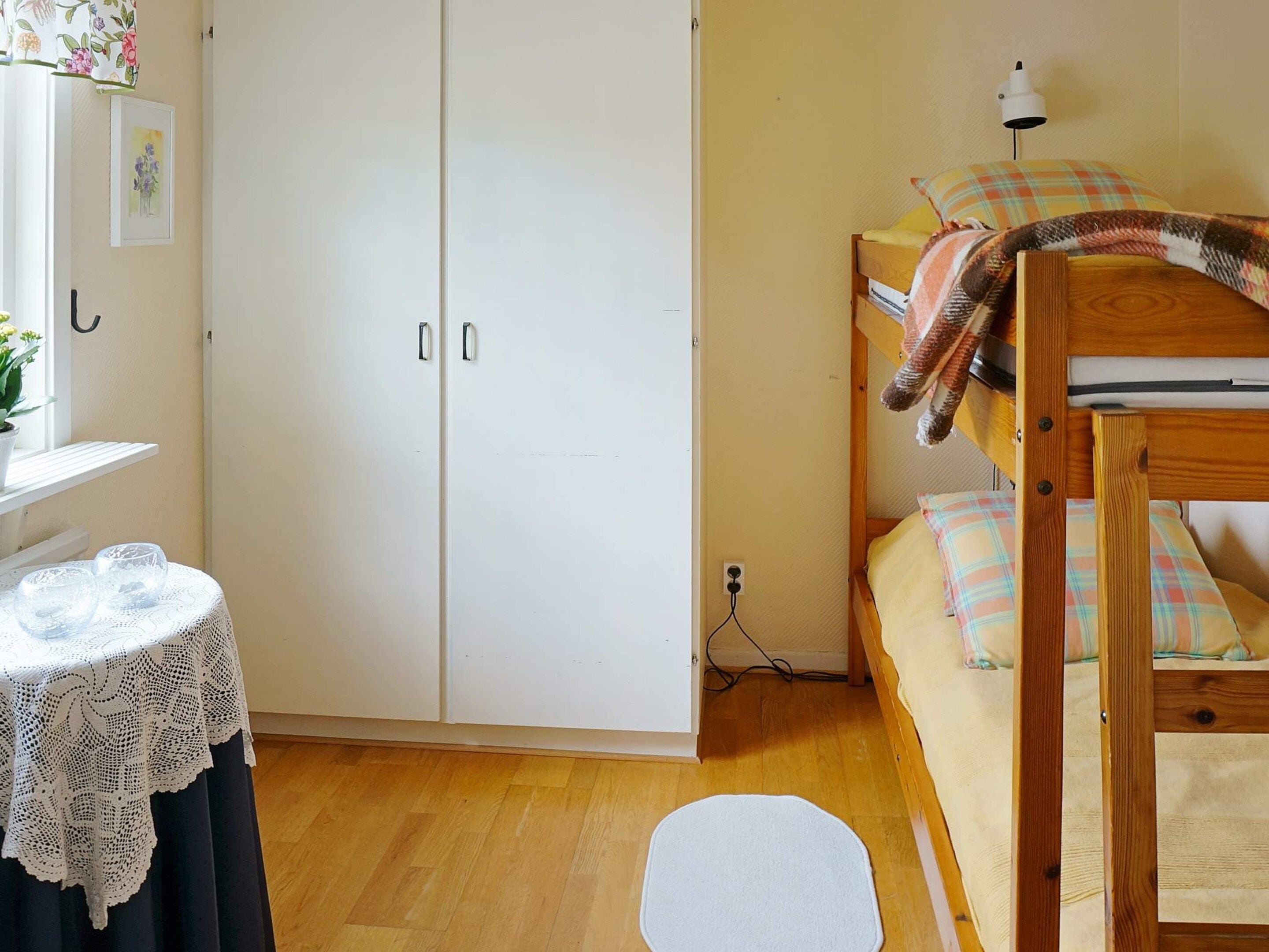 A bedroom with a bunk bed, a wardrobe, a bedside table with a lamp, and a small round rug.