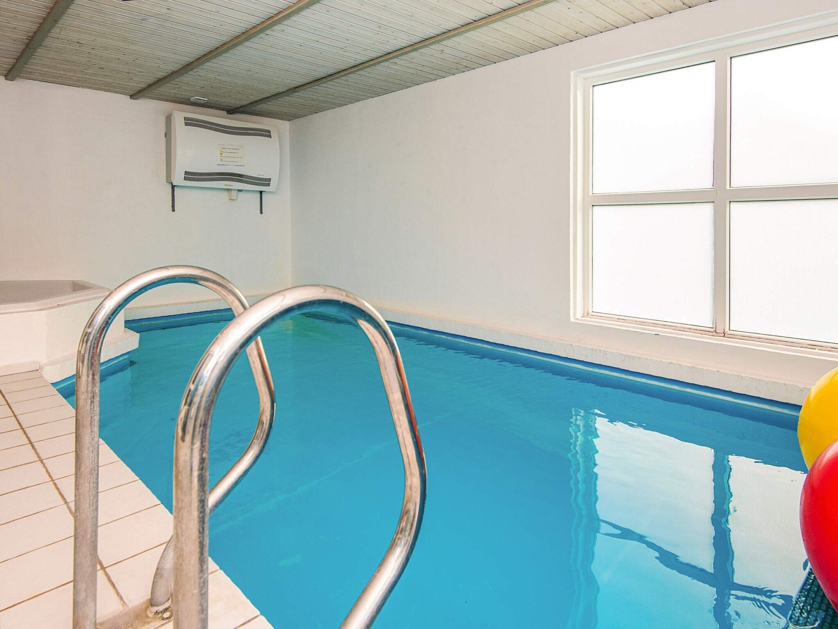 Une piscine intérieure avec des échelles en métal, un ventilateur de plafond et une fenêtre.