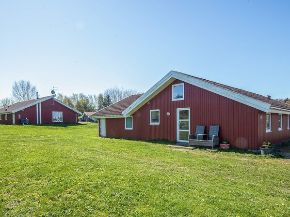 A red barn-style building with a sloped roof, a front door, and a small porch with chairs.
