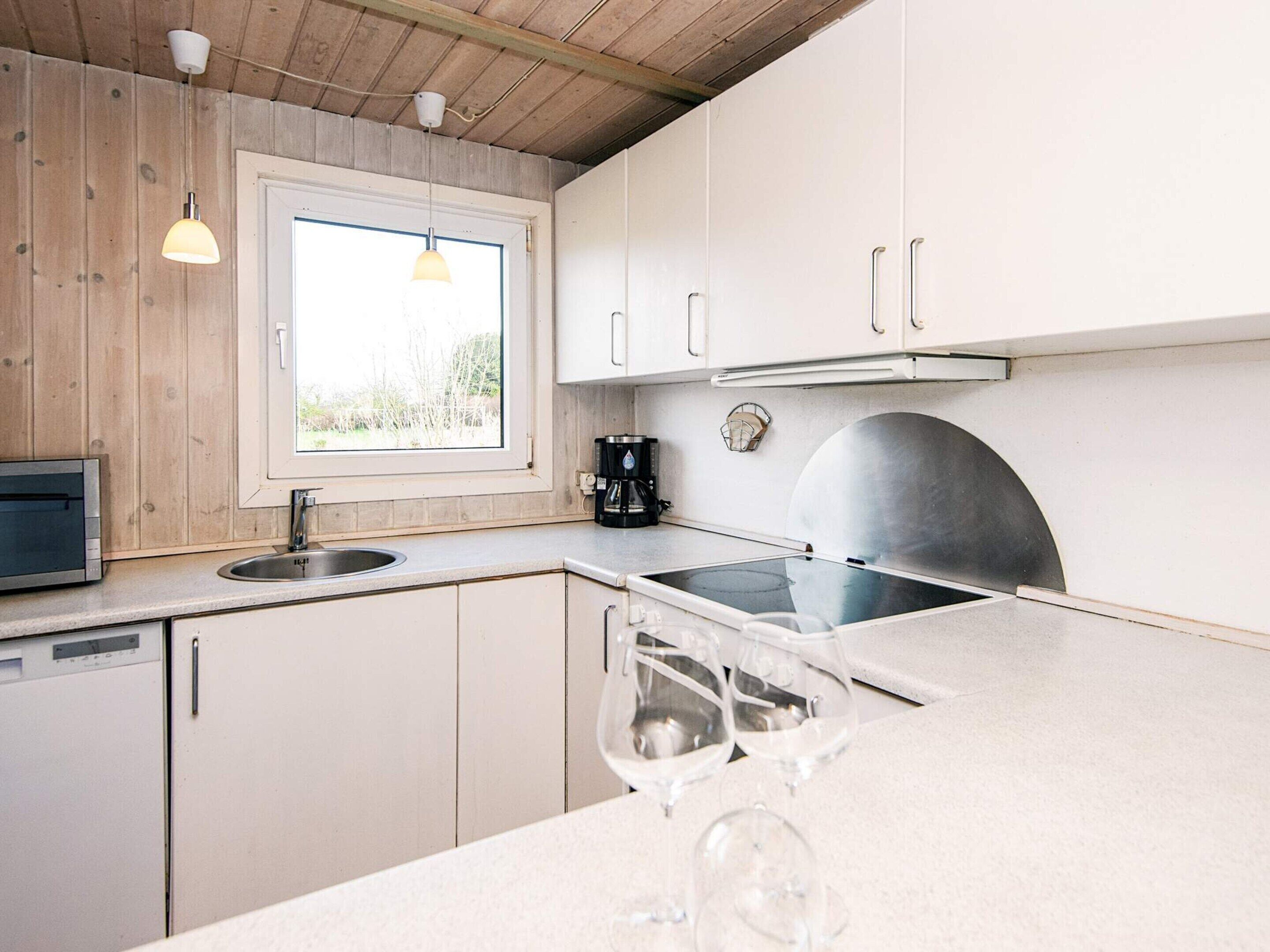 A kitchen with wooden cabinets, a window, a coffee maker, a toaster, and wine glasses on the counter.