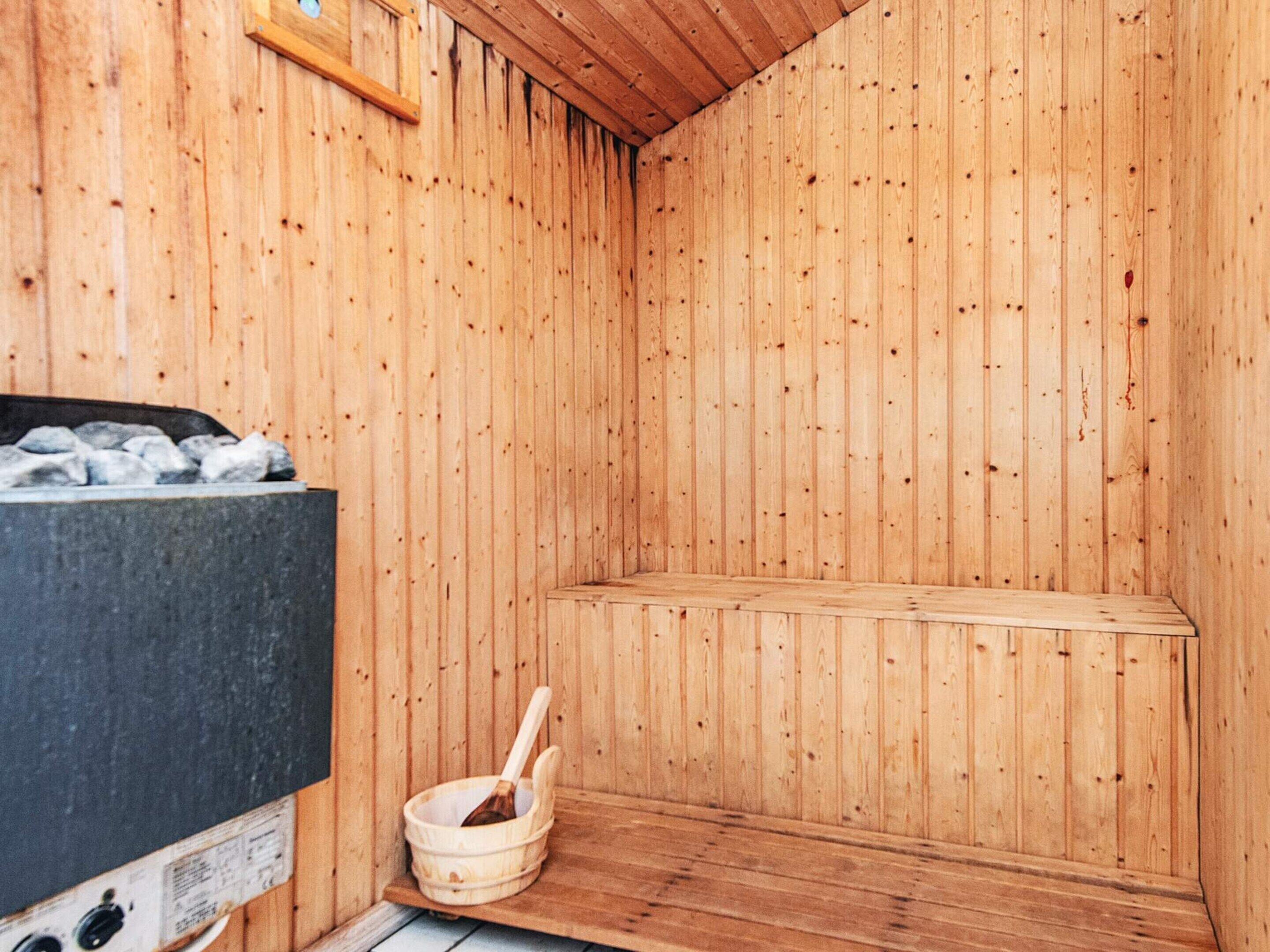 Un sauna avec des murs en bois, un banc, un récipient en pierre et un appareil de chauffage.