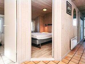 A wooden interior with a bed, a window, and a door leading to another room.