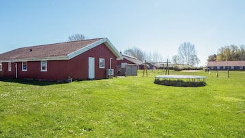 Une grange rouge avec un toit en pente, un trampoline et un champ d’herbe.
