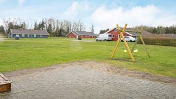 A paved area with a swing set, a brick building, and a red house in the background.