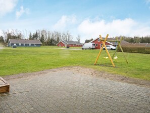 A paved area with a swing set, a brick building, and a red house in the background.
