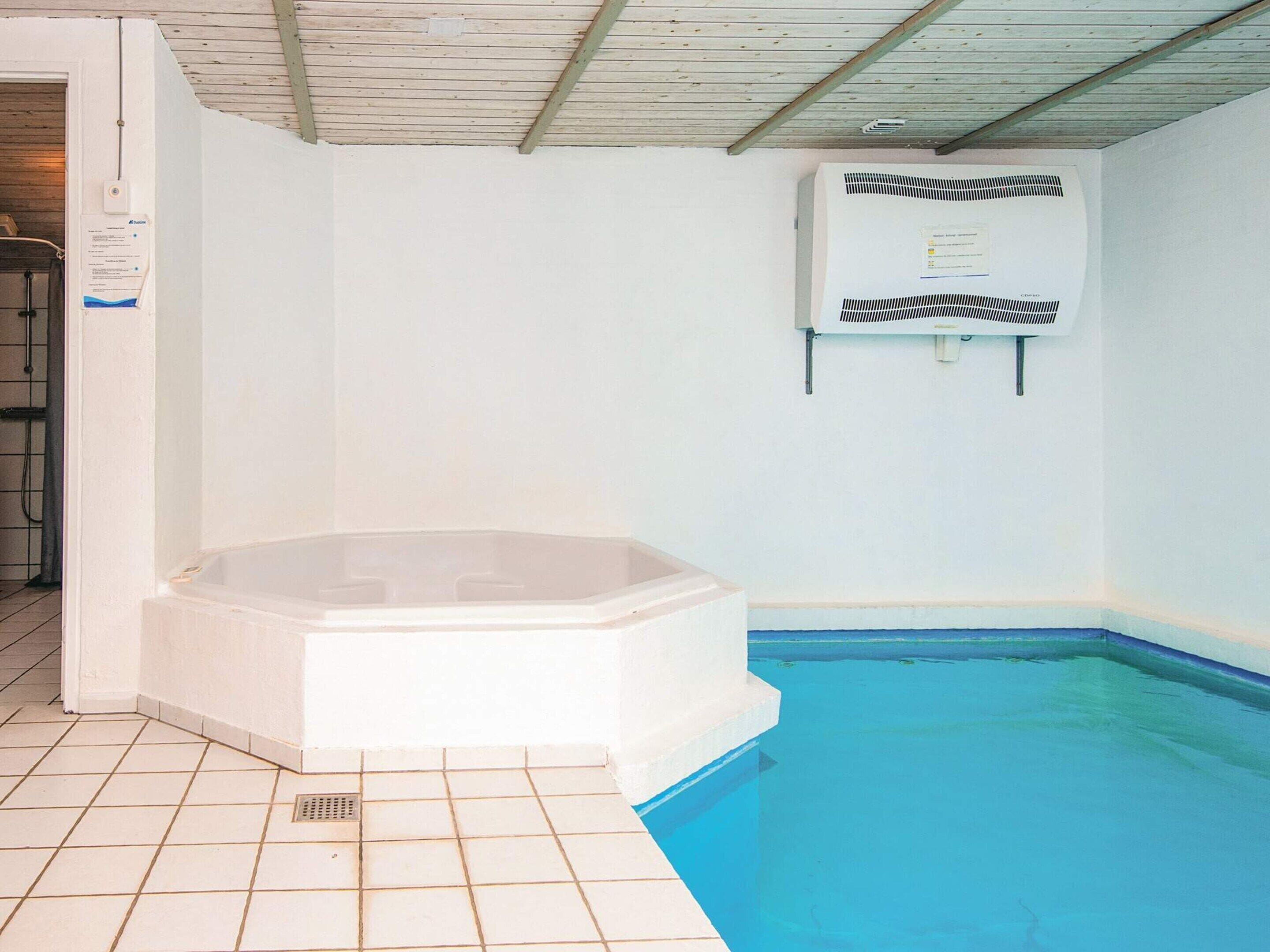A swimming pool with a hot tub adjacent to it, a ceiling fan, and a wall-mounted air conditioning unit.