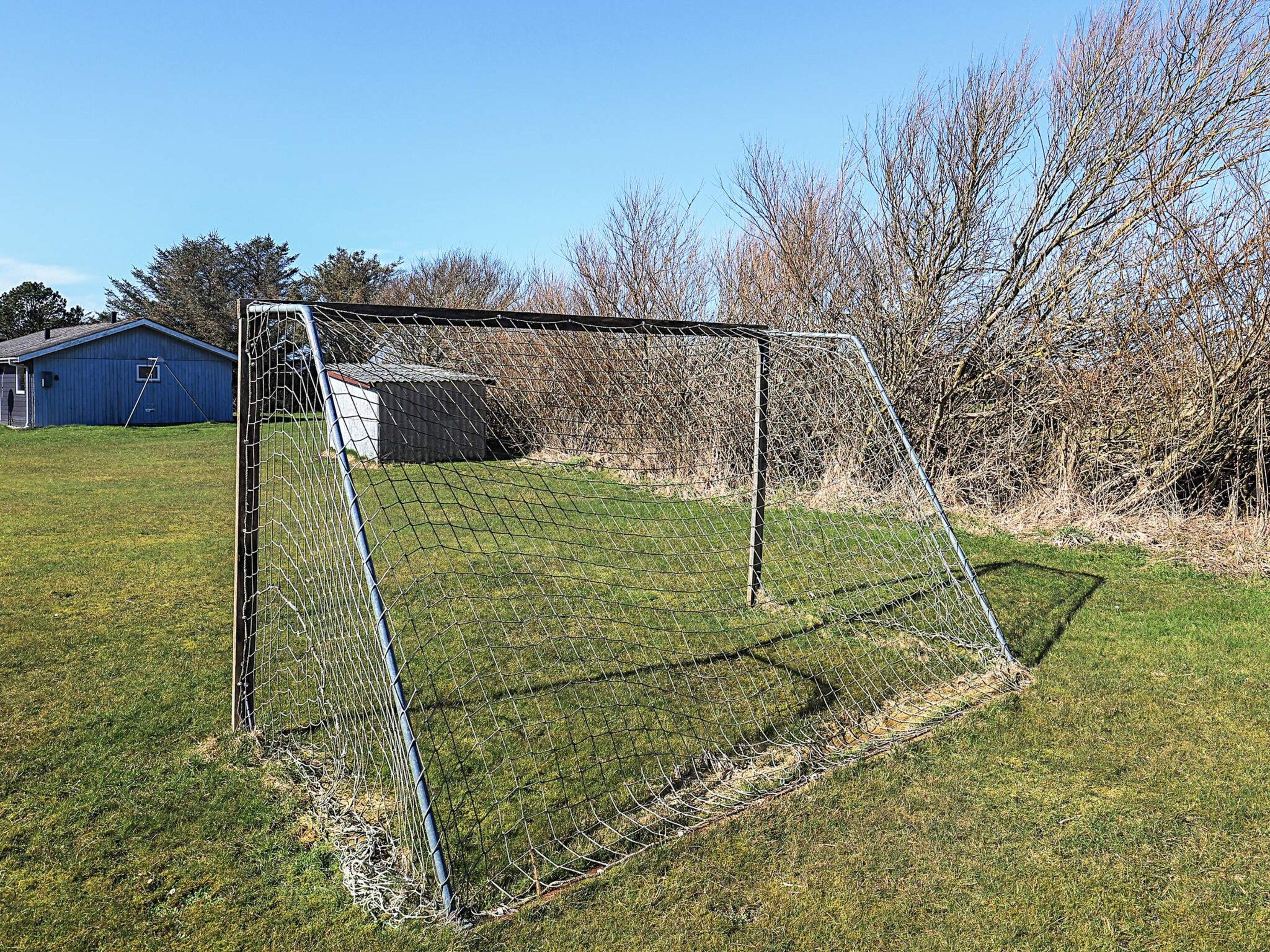 A soccer goal in a grassy field with a blue building in the background.