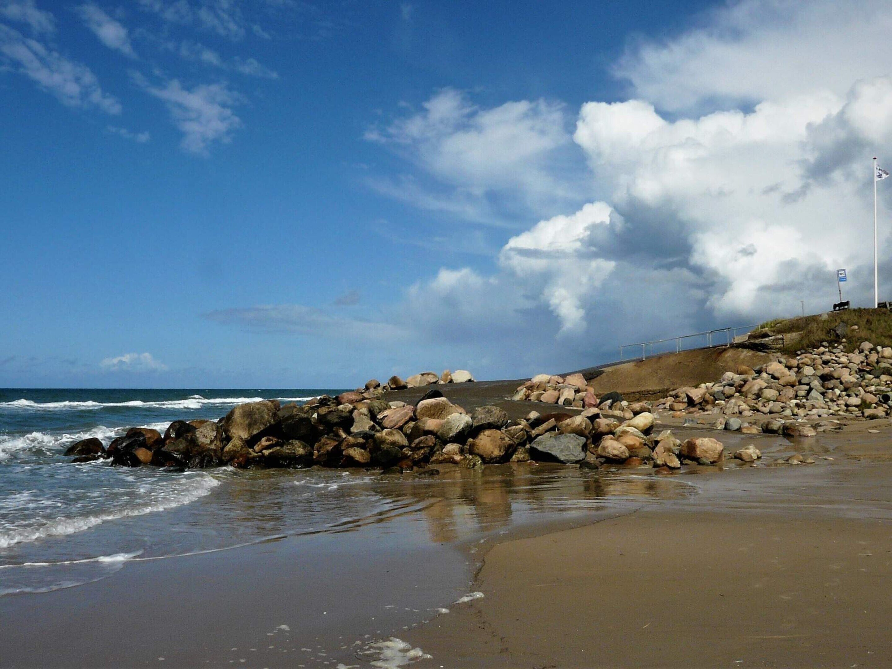 Una playa con rocas grandes, una orilla arenosa y un cielo despejado.