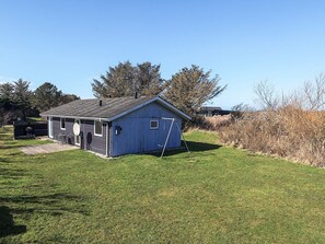 A small blue shed with a door and windows, a swing set, and a grassy yard. - 4 Person Holiday Home in Lokken (Lokken)