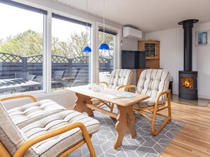 Una sala de estar acogedora con una mesa de madera, sillas a rayas, una chimenea y ventanas amplias.
