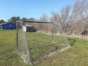 A soccer goal in a grassy field with a blue building in the background.