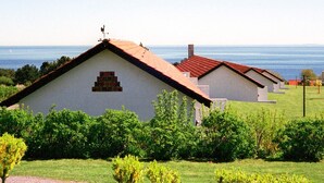 Una hilera de edificios blancos con techos rojos, presumiblemente parte de un complejo turístico o hotel, ubicada en una zona verde con vista al mar.