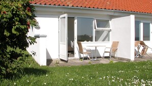 Un edificio blanco con techo de tejas rojas, puerta abierta y patio con dos sillas y una mesa.