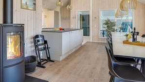 A modern kitchen with a central island, wooden walls, a black stove, and pendant lighting. - Holiday Home in Kappeln (Kappeln)