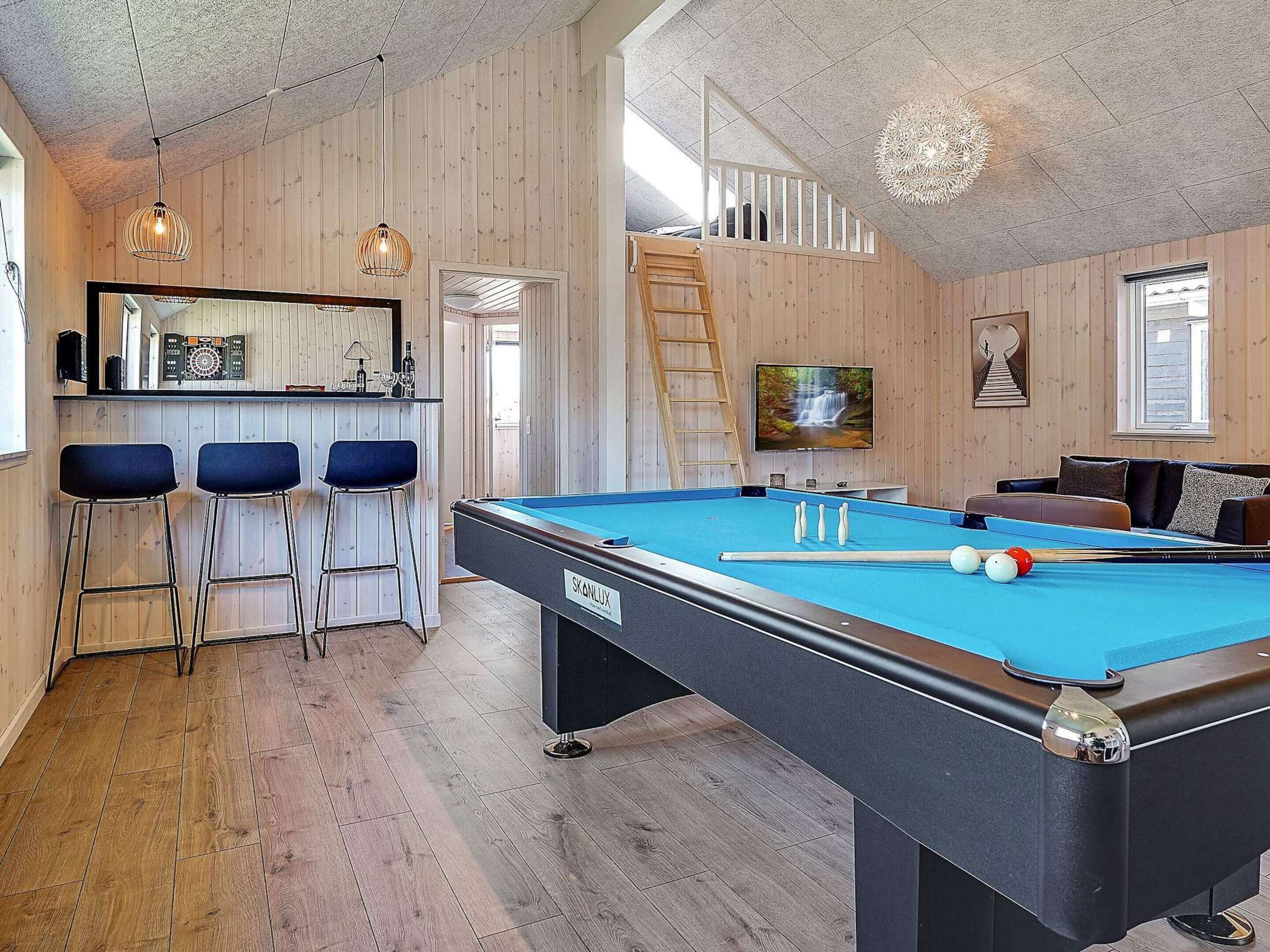 A pool table with a billiard cue, a bar area with stools, and a television mounted on the wall.