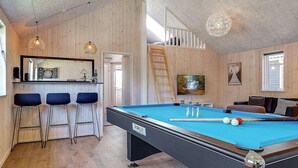 A pool table with a billiard cue, a bar area with stools, and a television mounted on the wall. - Holiday Home in Kappeln (Kappeln)