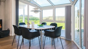 A modern dining area with a round table, black chairs, and a view of the outdoors through large windows.