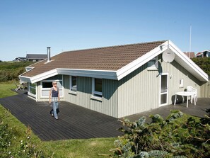 A single-story building with a sloped roof, a deck, and a small outdoor seating area.