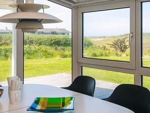 A dining area with a table, chairs, and a view of a grassy landscape through large windows.