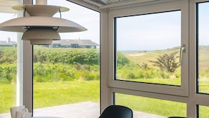 A dining area with a table and chairs, a pendant light, and a view of a grassy landscape through large windows.