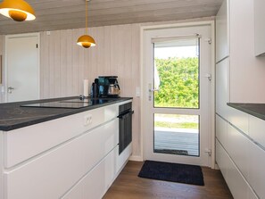 A compact kitchen with a built-in stove, a coffee maker, and a door leading to a balcony with a view of greenery.