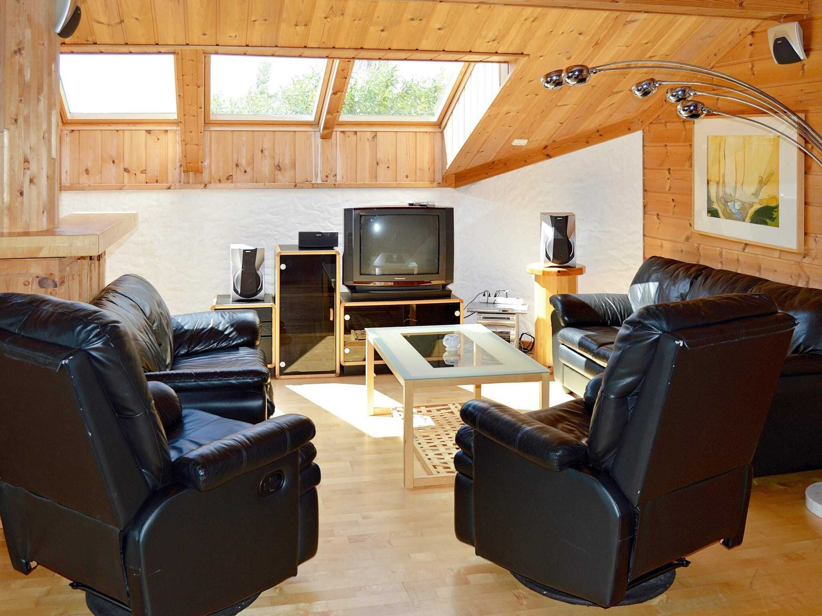 A cozy living room with a TV, leather chairs, a coffee table, and wooden walls.