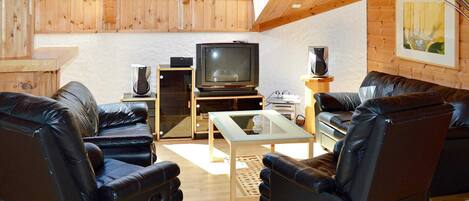 A cozy living room with a TV, leather chairs, a coffee table, and wooden walls.