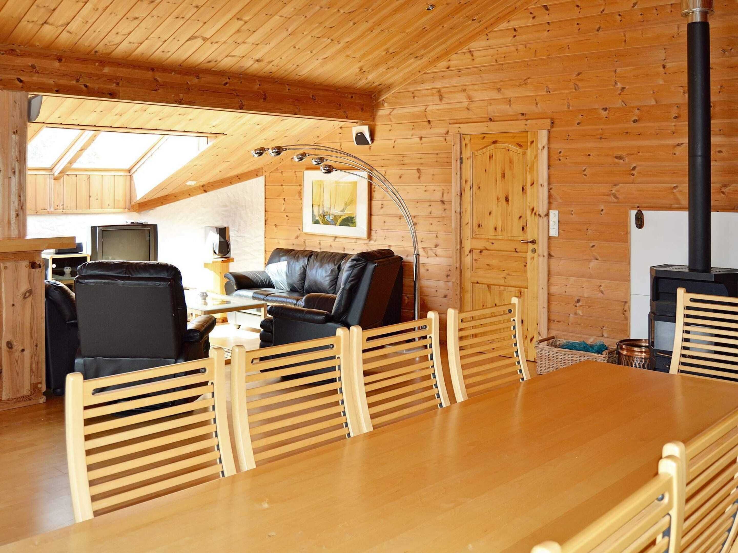 L’intérieur d’un chalet en bois comprend une table à manger, des chaises, un canapé, un téléviseur, une cheminée et une lucarne.