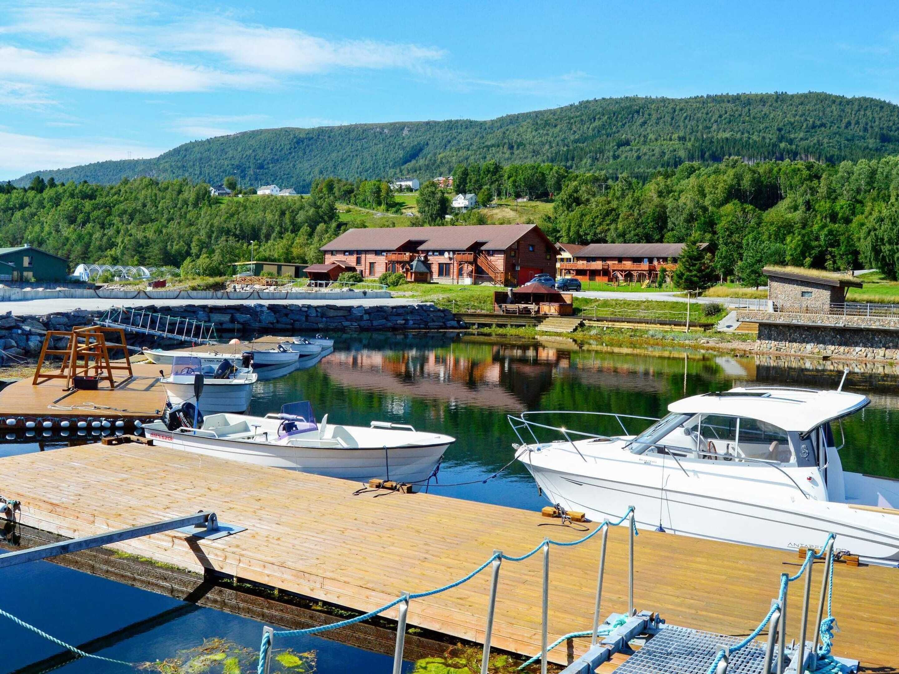 A marina with boats docked, a wooden dock, and a building with a red roof in the background.