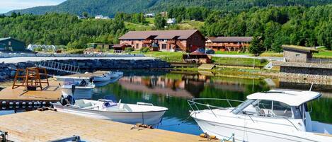 A marina with boats docked, a wooden dock, and a building with a red roof in the background.