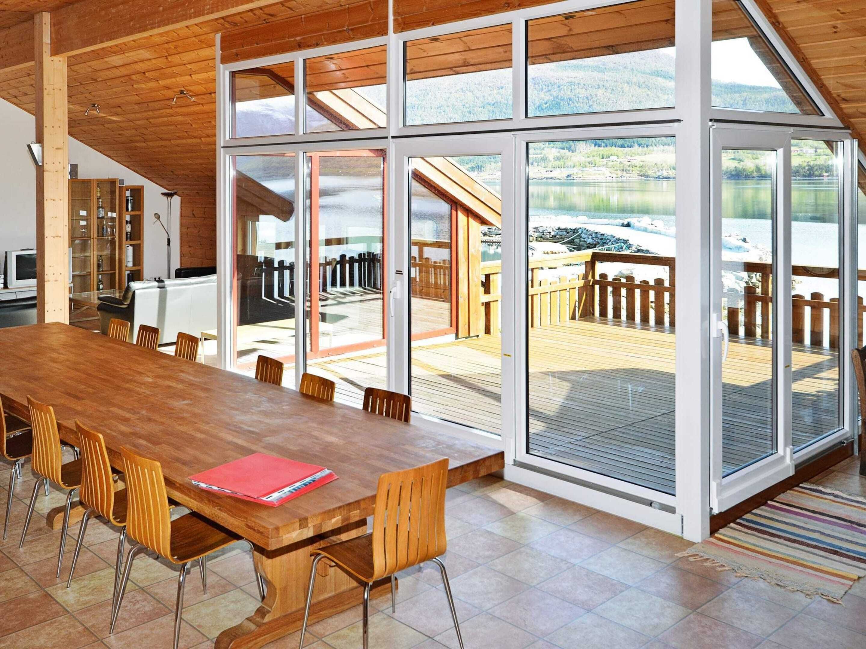 A spacious dining area with a large wooden table and chairs, large sliding glass doors leading to an outdoor deck with a view of a lake and mountains.