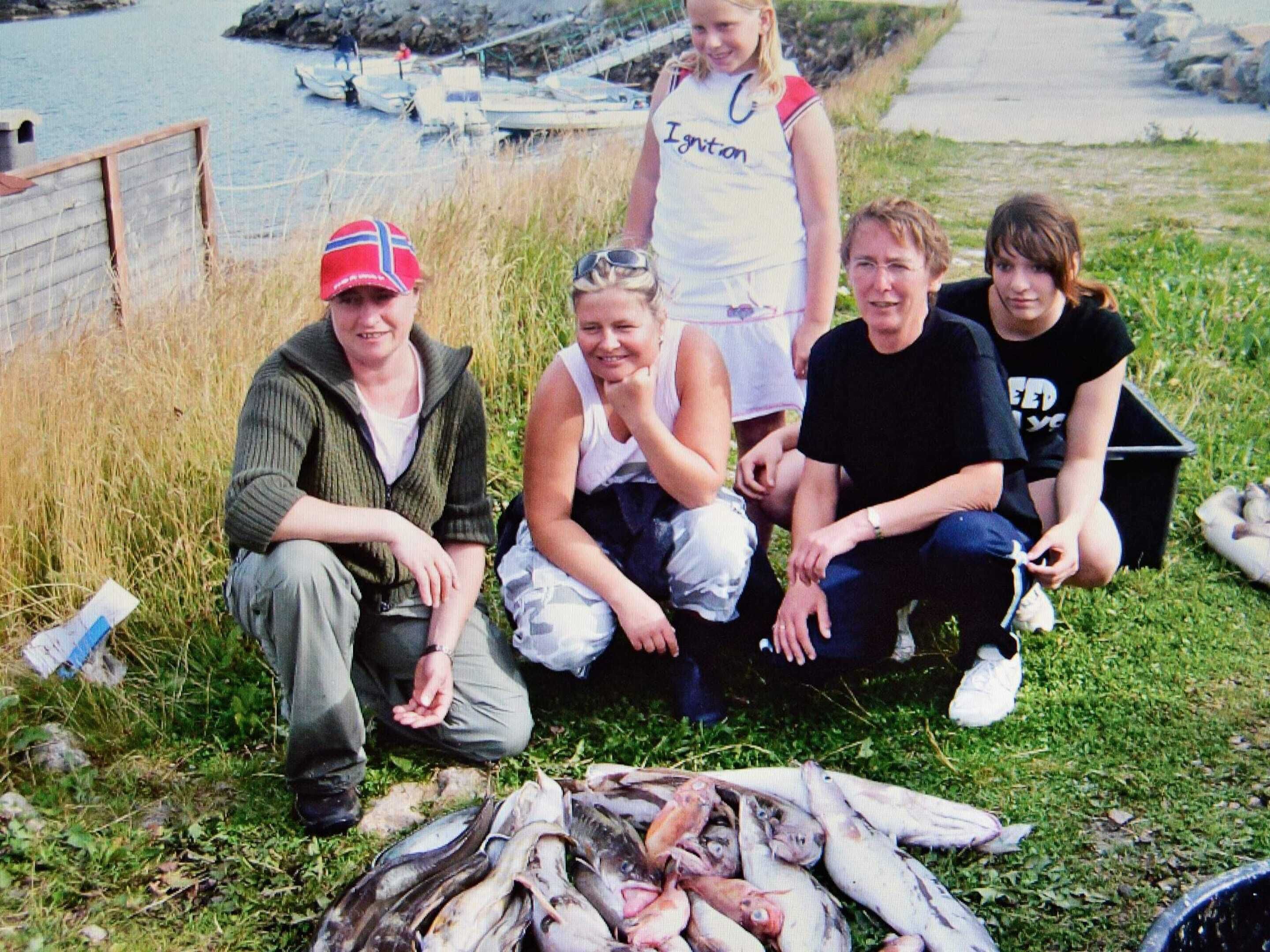 A group of people sitting on grass near a body of water with boats in the background.